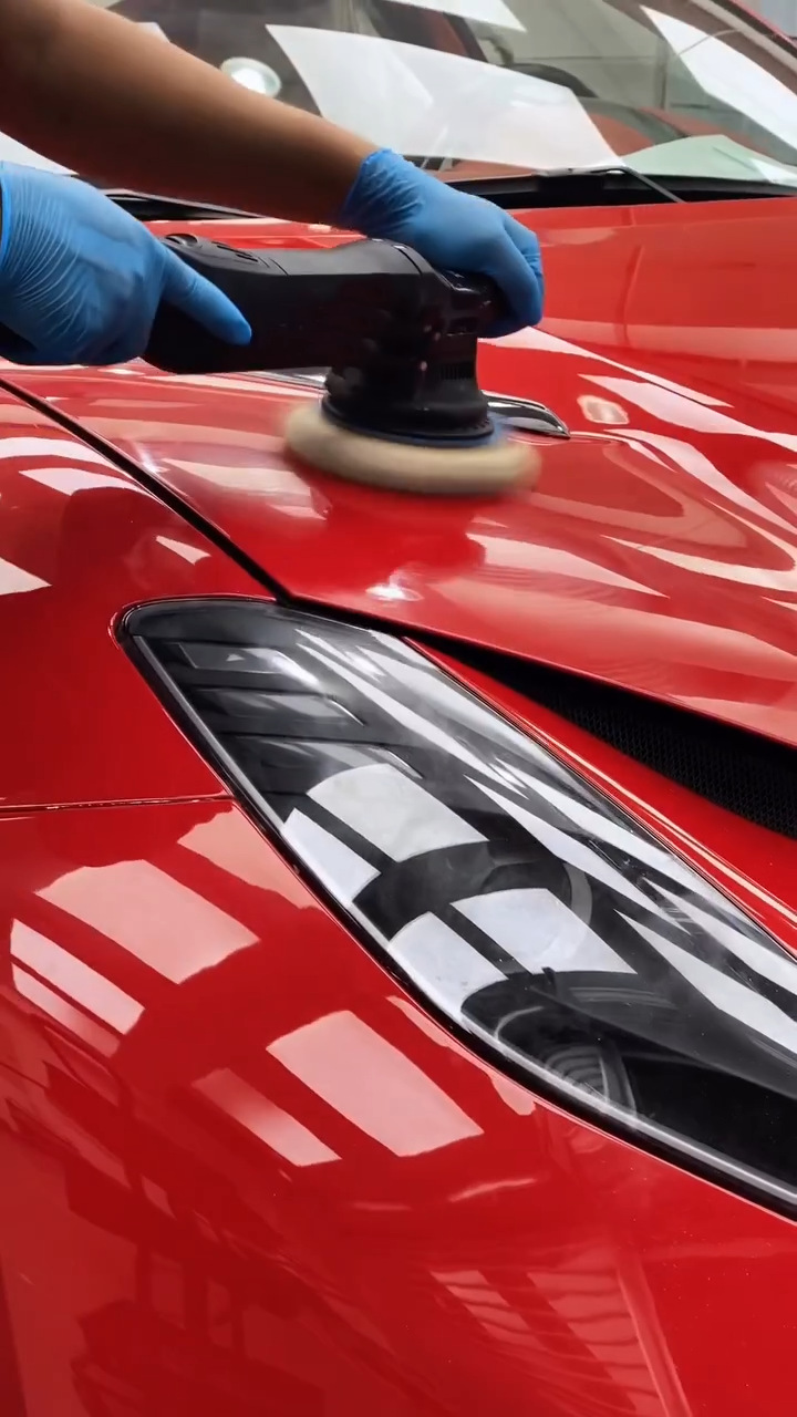 Gloved hands machine-polishing the bonnet of a red car